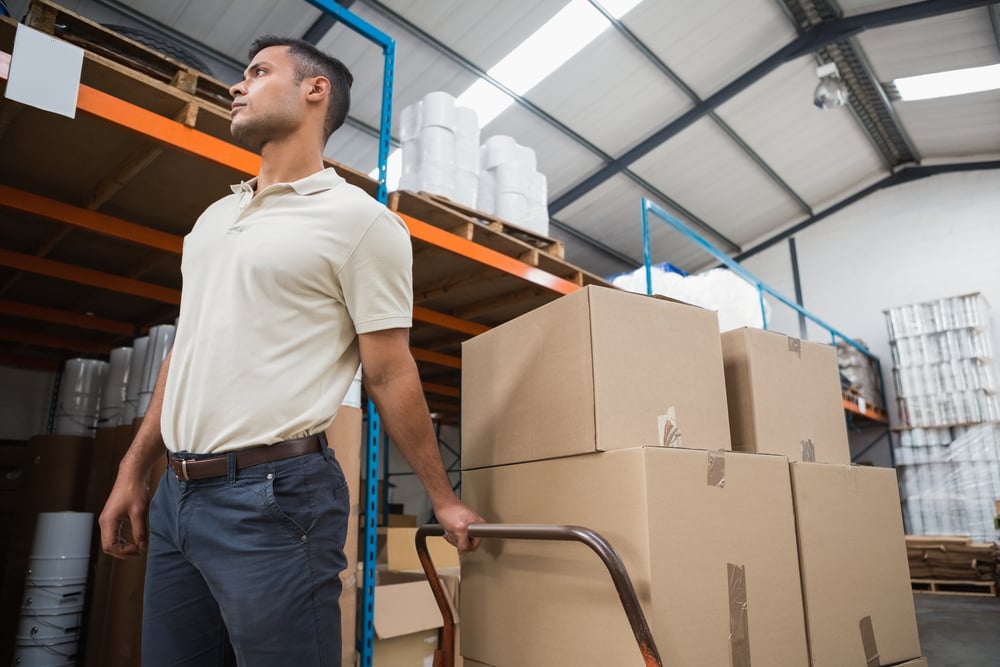 Worker pushing trolley with boxes in warehouse